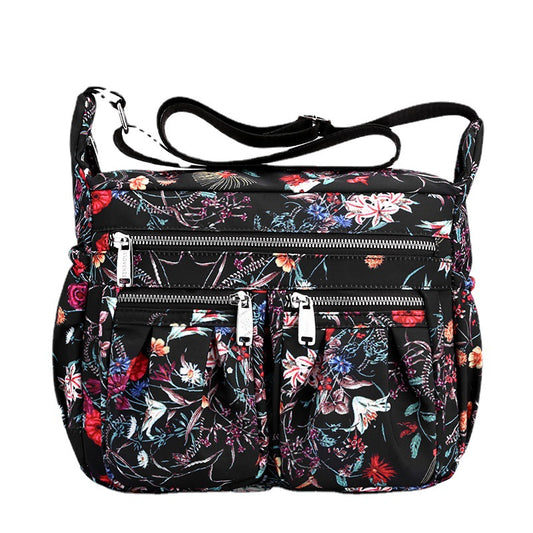 Large-capacity crossbody bag in black floral print with several front zip compartments.