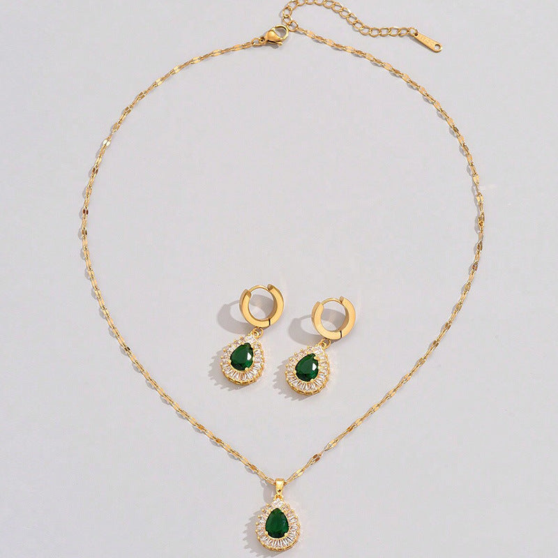 Gold necklace and earrings with green gemstones on a light gray background