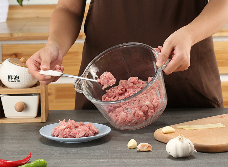 Person transferring ground meat from a glass bowl to a plate in a kitchen setting.