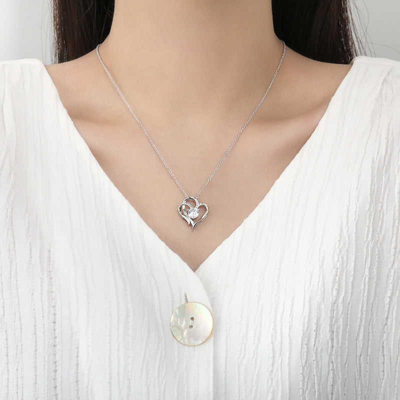 Silver necklace with a heart-shaped pendant worn by a person in a white shirt.