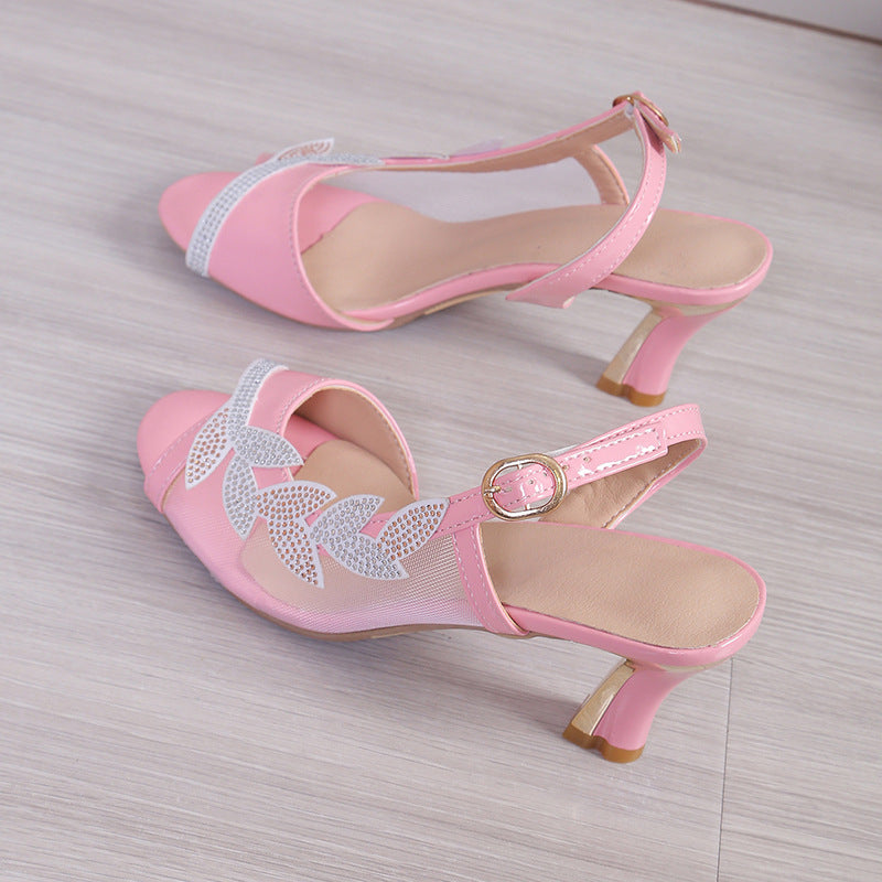 Pair of pink high-heeled shoes with decorative elements on a light wooden floor.