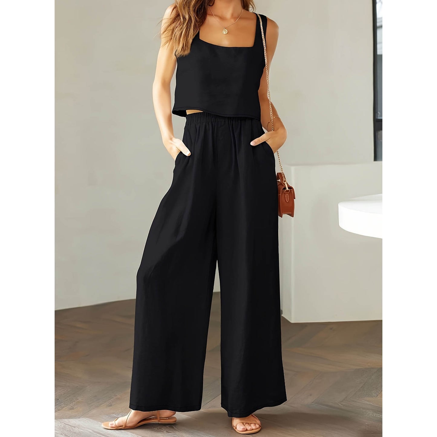 Woman wearing a black jumpsuit standing indoors with a neutral background