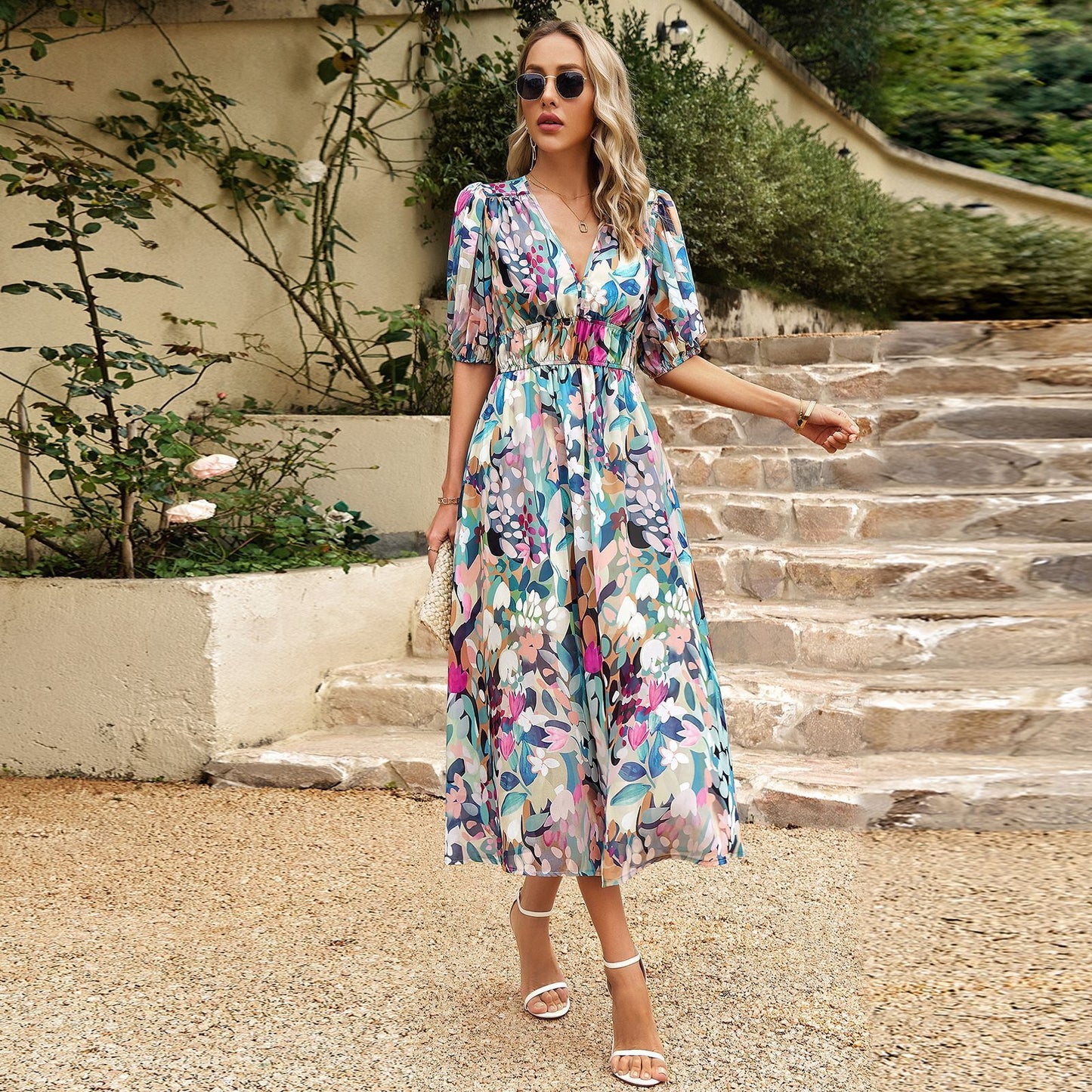 Woman in a floral dress standing on stone steps with greenery in the background