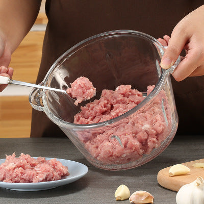 Glass container with ground meat and a spoon, with a person in the background.