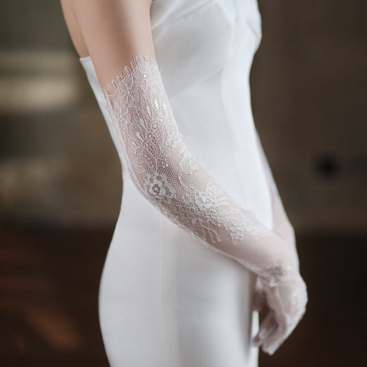 Close-up of a lace glove worn with a white outfit against a blurred background