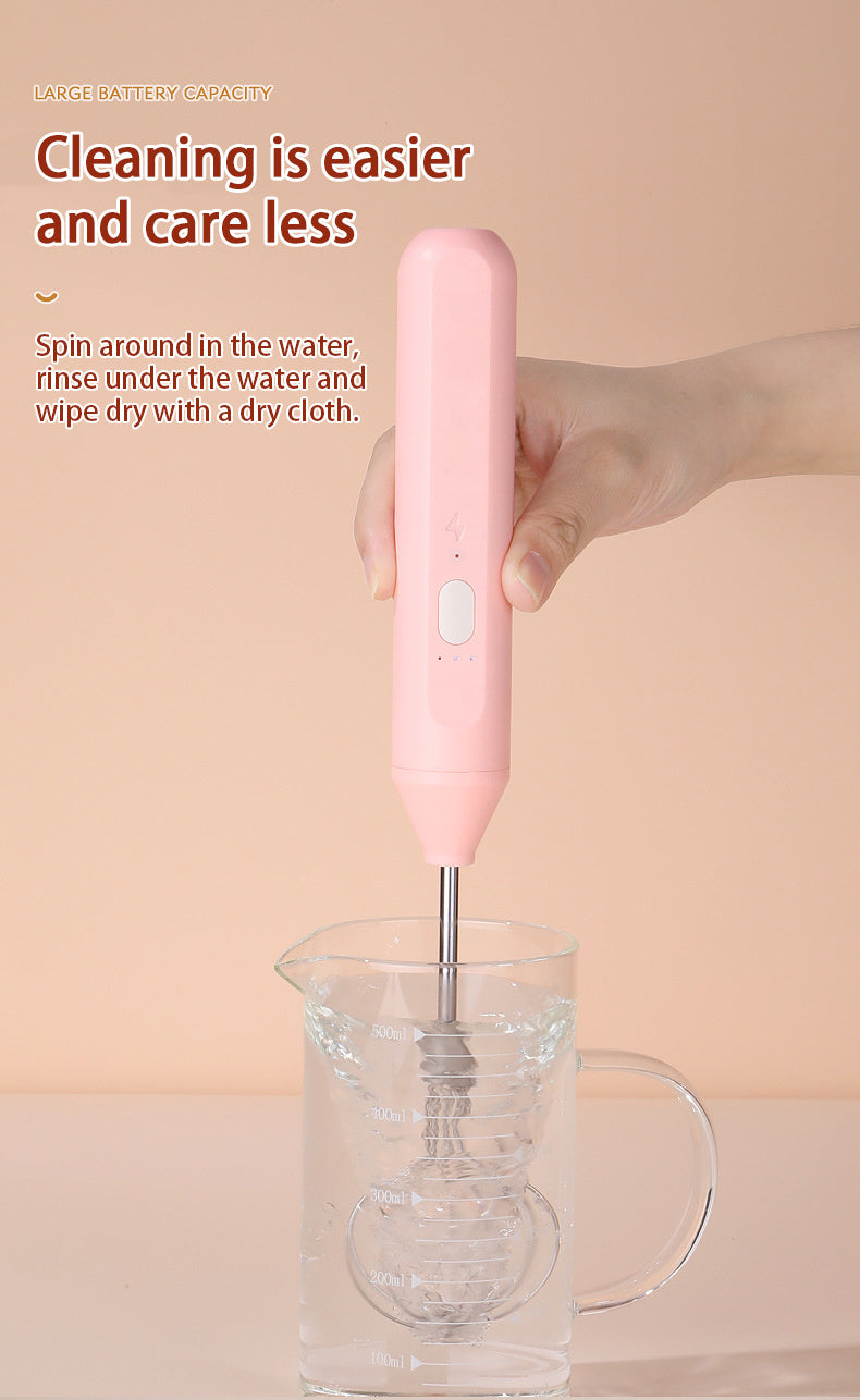 Pink hand mixer being used to mix ingredients in a glass bowl with a beige background.
