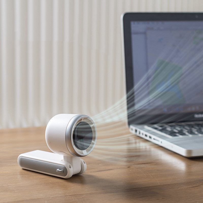 White cylindrical device emitting a beam towards a laptop on a wooden surface.