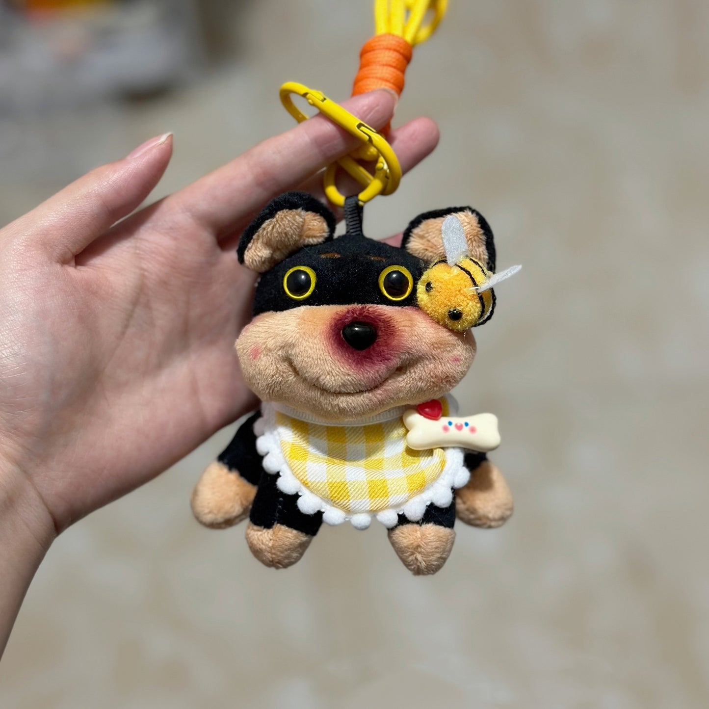 Plush keychain shaped like a dog in a bee costume held by a hand against a blurred background