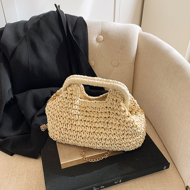 Beige woven handbag on a black book with a black coat draped over a beige armchair.