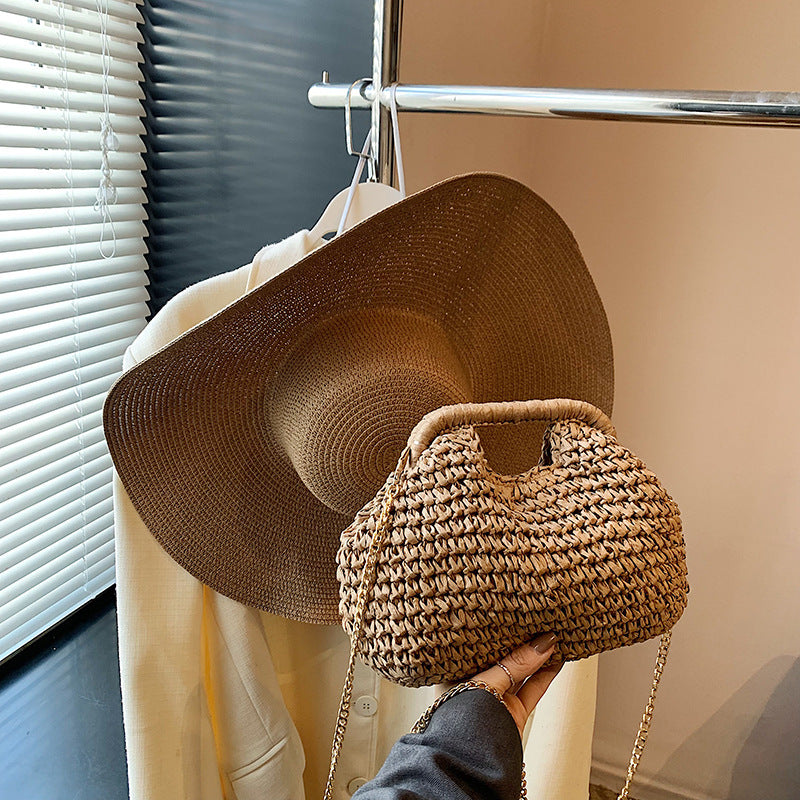 Woven hat and handbag held by a person in front of a mirror.