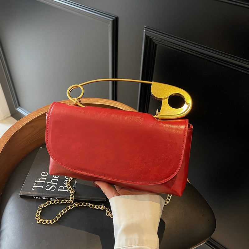 Red handbag with a gold handle and chain held by a person on a chair.