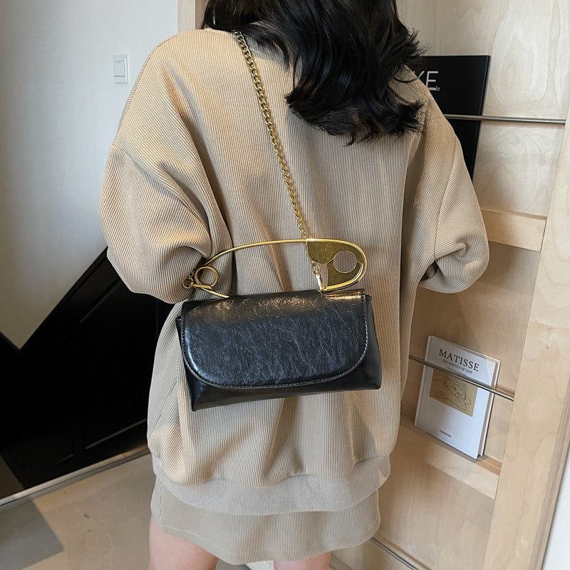 Person wearing a beige jacket with a black handbag featuring a gold clasp.