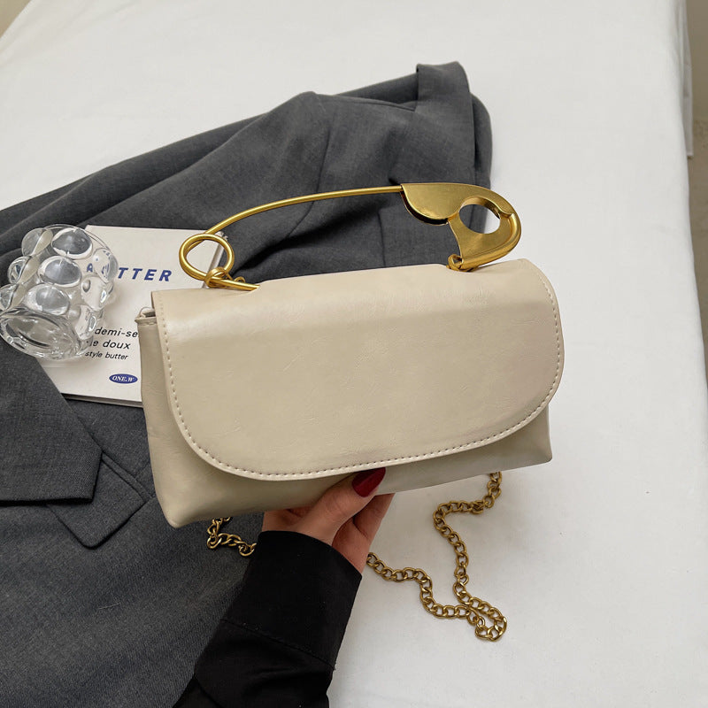 Beige handbag with gold chain and clasp held by a hand on a white surface.
