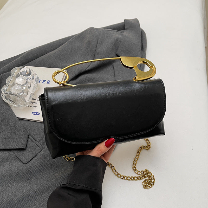 Black handbag with gold chain and handle held by a hand on a white surface