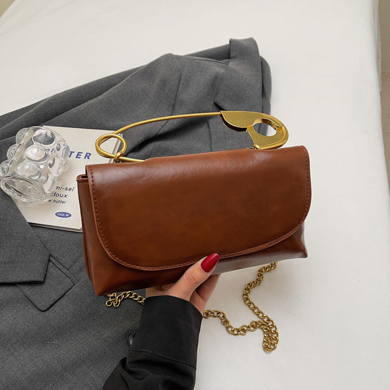 Brown handbag with gold chain and handle held by a hand on a white background