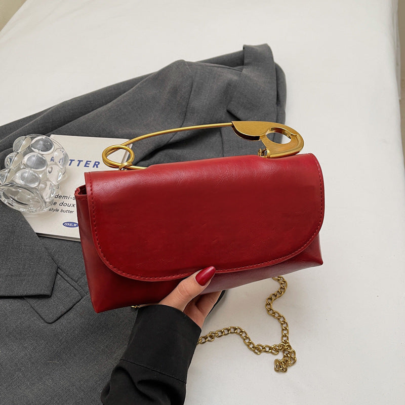 Red handbag with gold handle and chain on a white surface