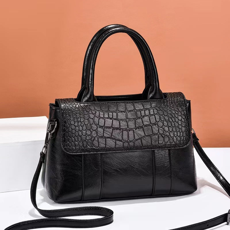 Black handbag with crocodile texture on a white surface with a brown background