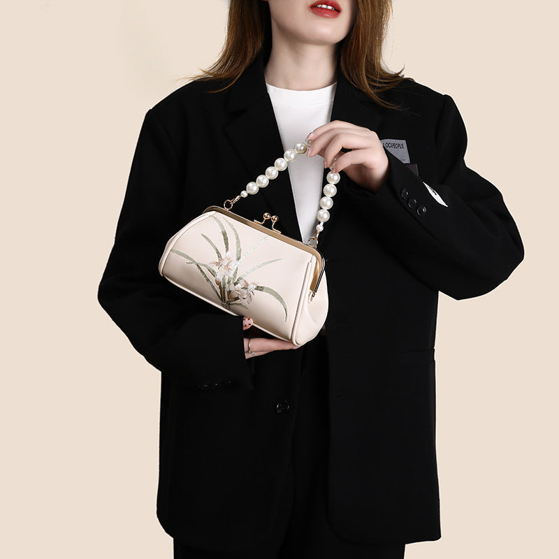 Person holding a pearl-handled handbag with a floral design against a beige background
