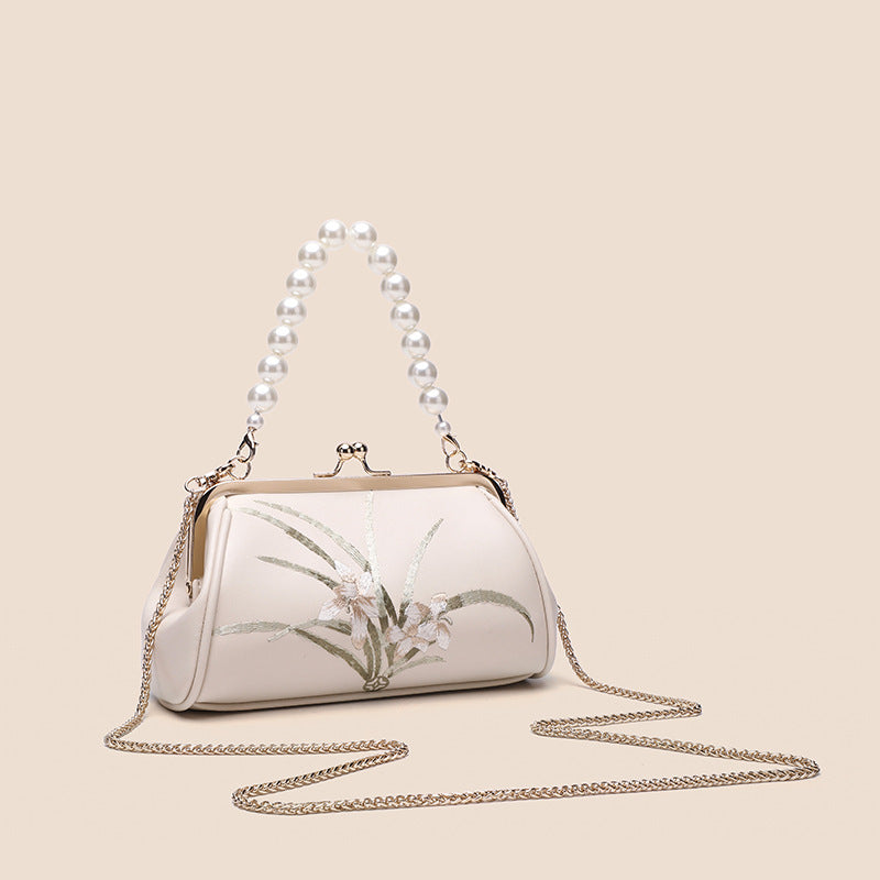 White handbag with floral design and pearl chain on a beige background