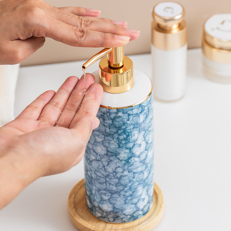 Person using a blue marbled soap dispenser with gold pump on a white surface.