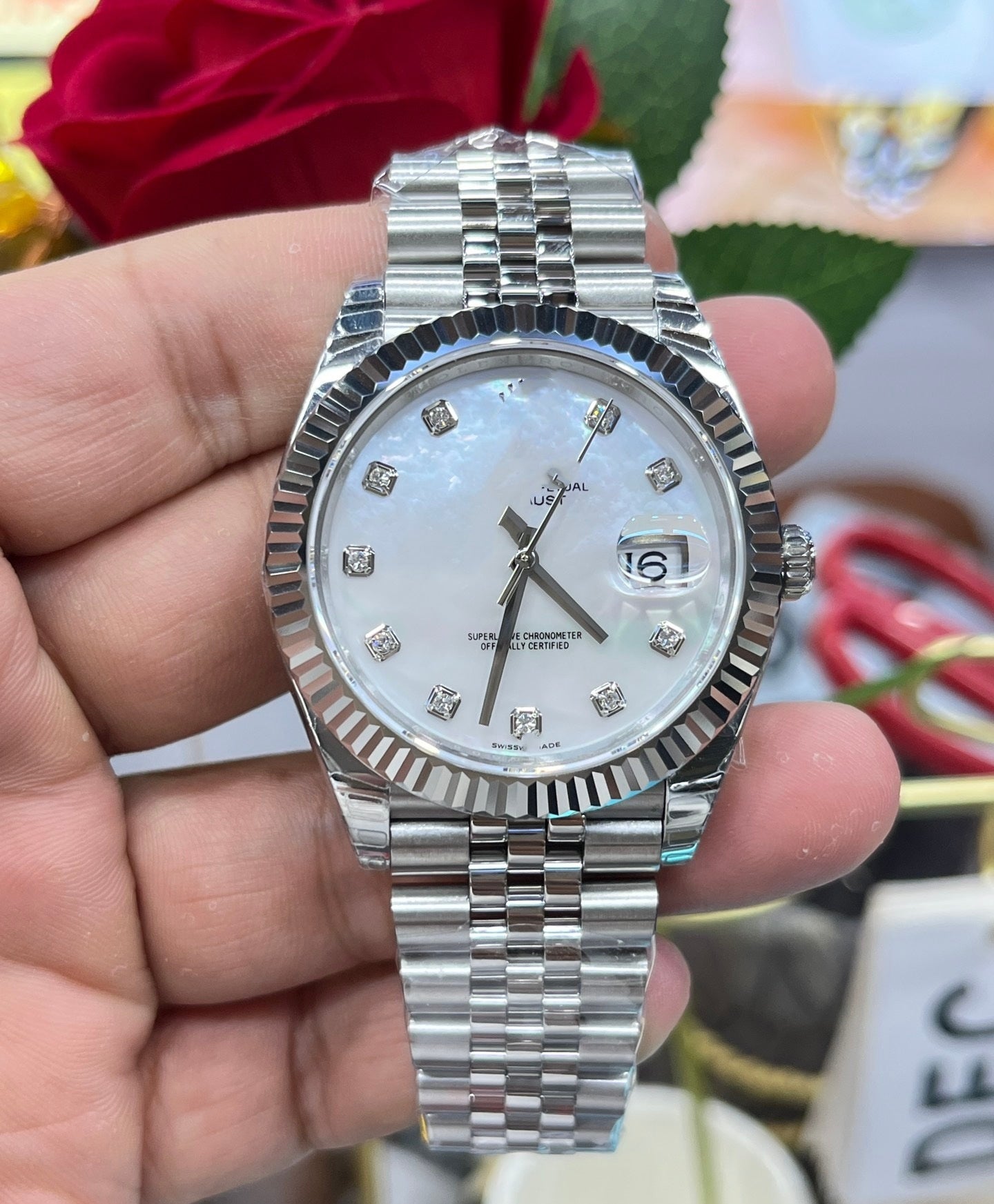 Silver watch with a white face held in a hand, with a blurred background