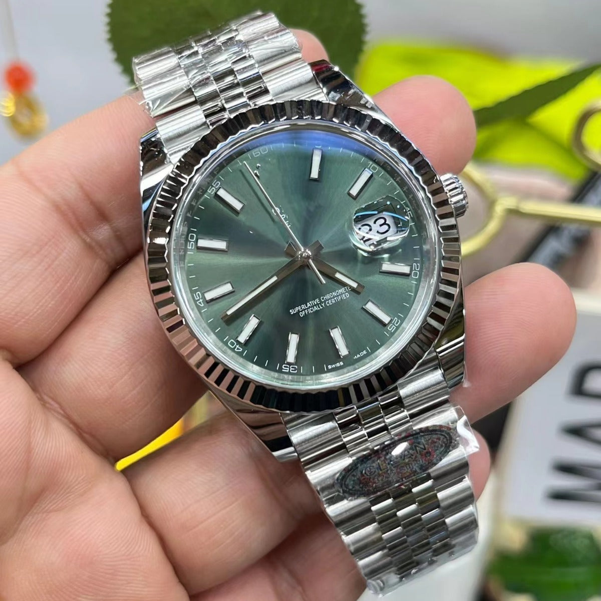 Silver watch with a green face held in a hand against a blurred background