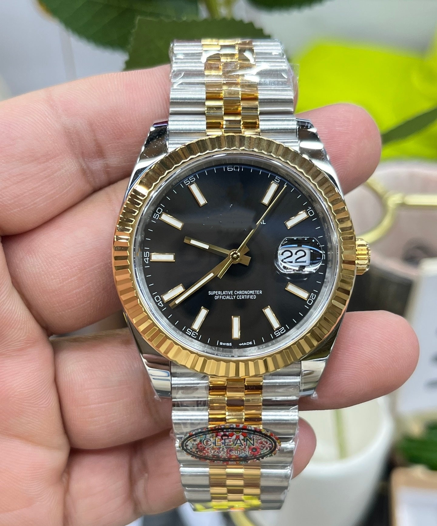 Two-tone silver and gold watch with black dial held in a hand against a blurred background