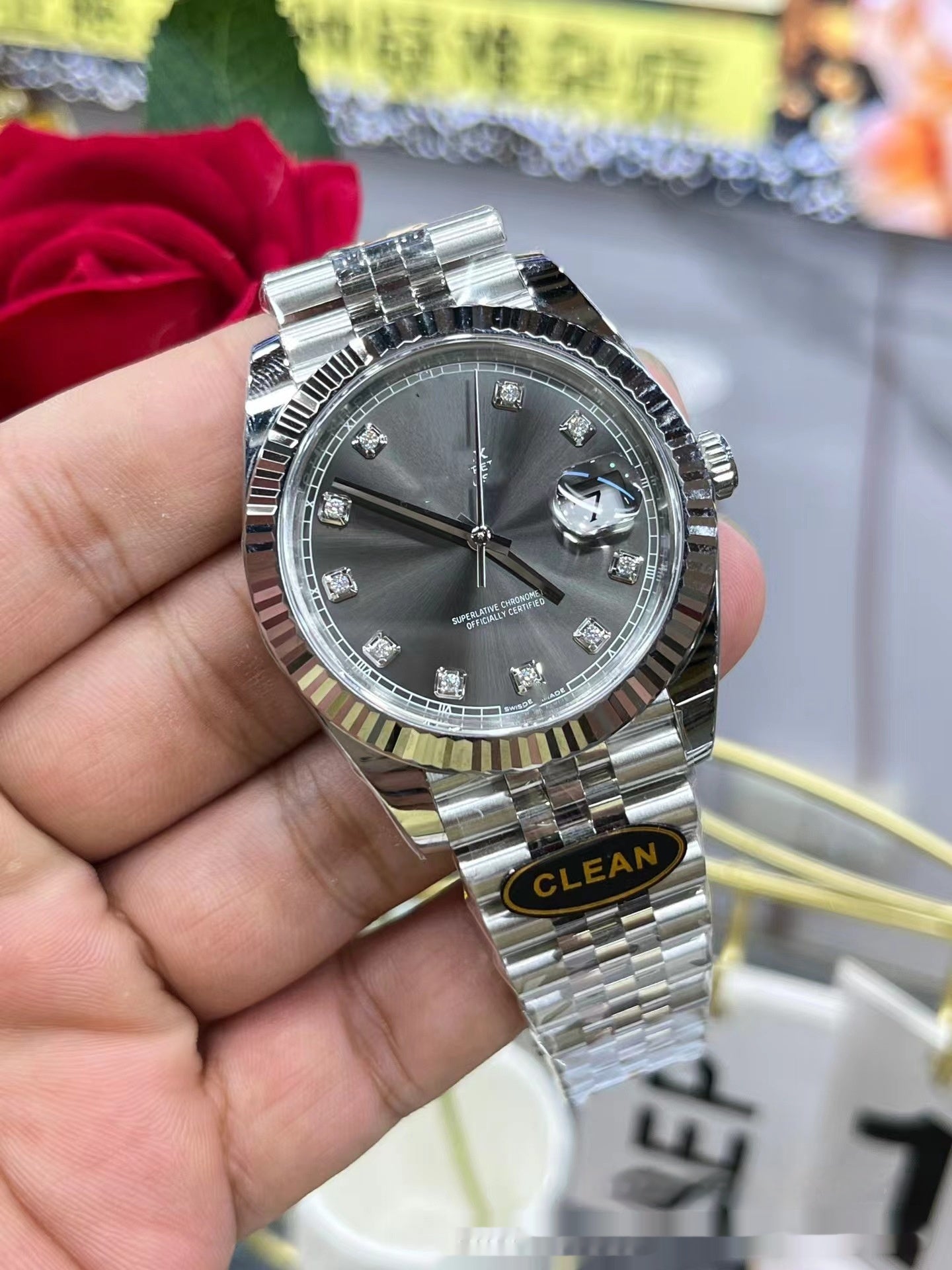 Silver watch with a gray face held in a hand, blurred background