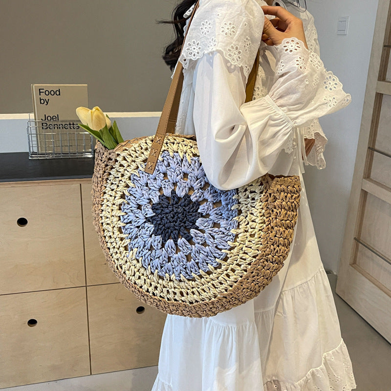 Person holding a round woven bag with a blue floral pattern, wearing a white dress.