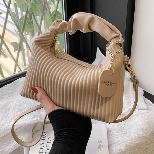 Beige handbag held by a hand with a blurred background
