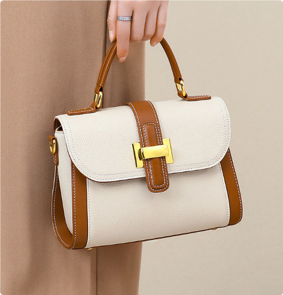 Beige handbag with brown accents held by a hand against a beige background