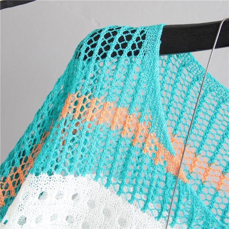 Knitted shawl with a geometric pattern on a hanger against a gray background