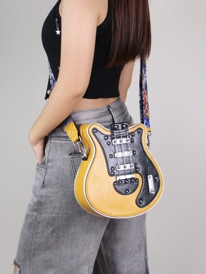 Yellow guitar-shaped crossbody bag with black guitar face, stud accents, and guitar strap