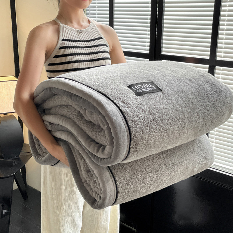 Person holding a folded gray blanket with a brand label in a room.