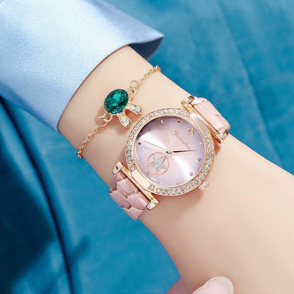 Rose gold watch with pink strap and green gemstone on a wrist against a blue fabric background