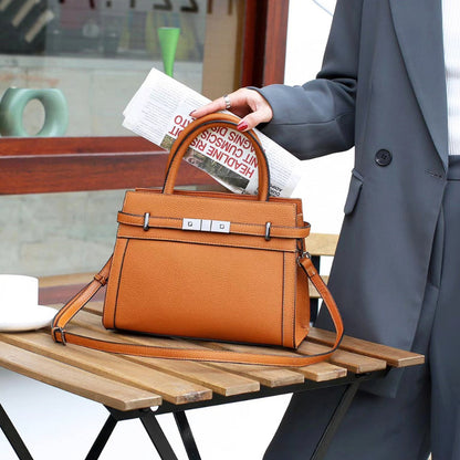Brown leather handbag on a wooden table with a person in a gray coat holding a newspaper.
