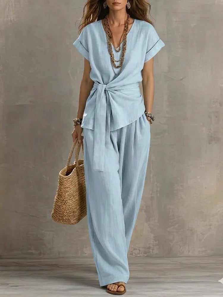 Woman wearing a light blue jumpsuit holding a straw bag against a neutral background