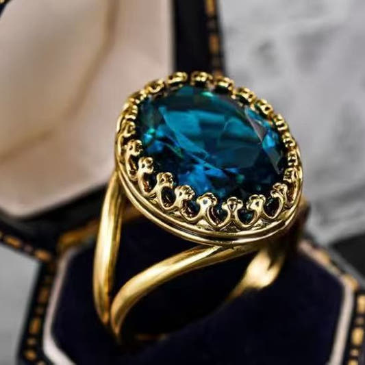 Gold oval ring with ornate lace-like bezel and faceted teal-blue gemstone center
