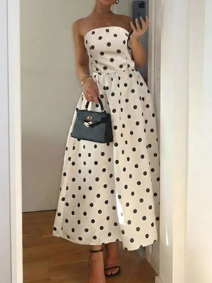 Woman wearing a white strapless dress with black polka dots, holding a black handbag, standing in front of a mirror.