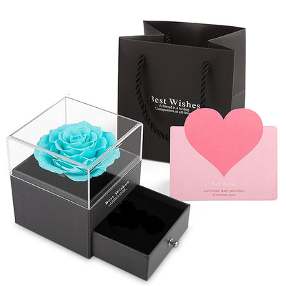 Blue rose in a clear box with a black gift bag and pink heart card on a white background
