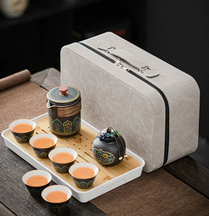 Tea set with teapot and cups on a tray next to a gray travel case.