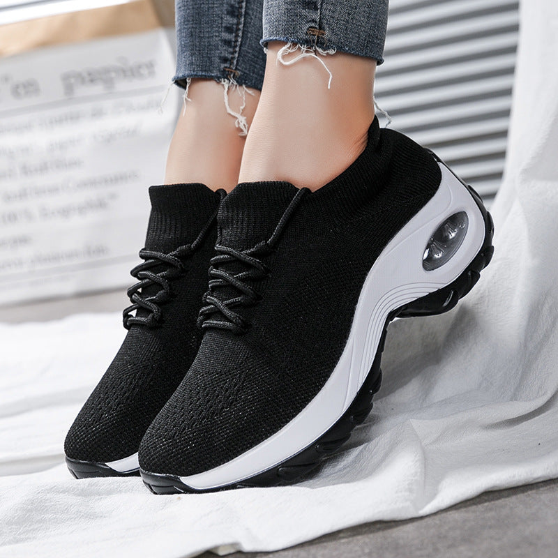 Black athletic shoes with white soles worn by a person on a light gray background