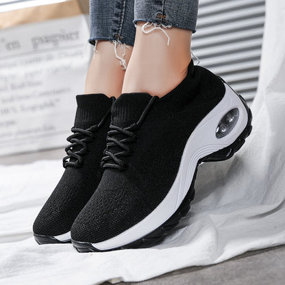 Black athletic shoes with white soles worn by a person on a light gray background