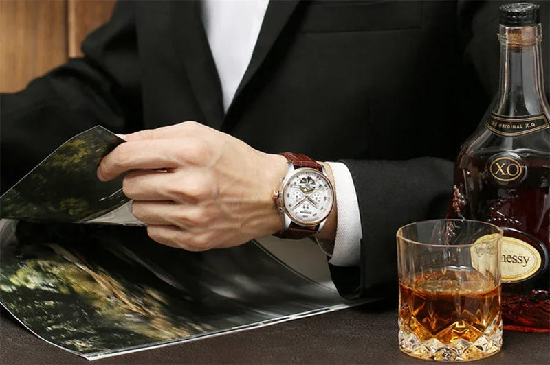 Automatic mechanical watch with silver case, dark leather strap on wrist.
