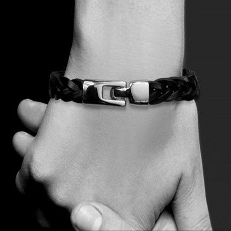 Black braided leather bracelet with a metal clasp on a wrist against a dark background