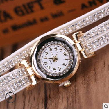 Watch with a white strap and gold casing on a wooden surface