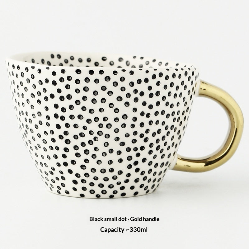 Ceramic mug with black dot pattern and gold handle on a white background