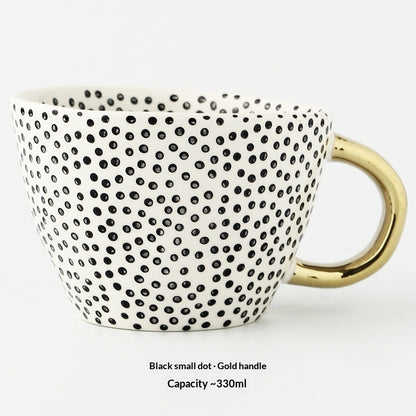 Ceramic mug with black dot pattern and gold handle on a white background