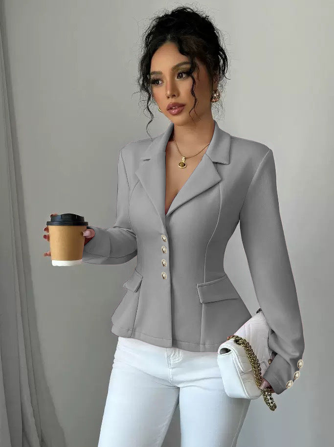 Woman in a gray blazer holding a coffee cup and a white handbag against a plain background