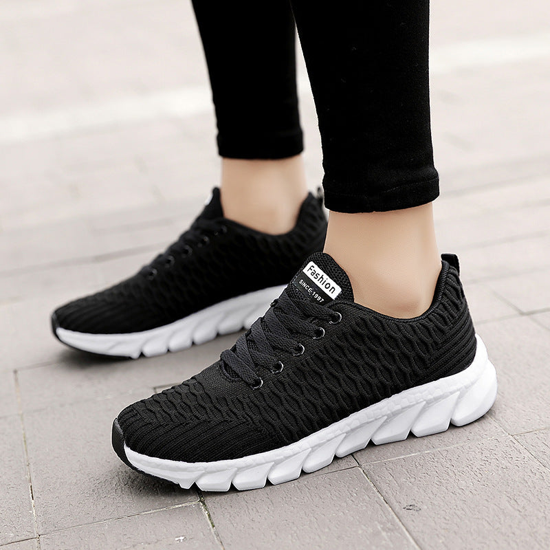 Black sneakers with white soles worn by a person on a light gray pavement.